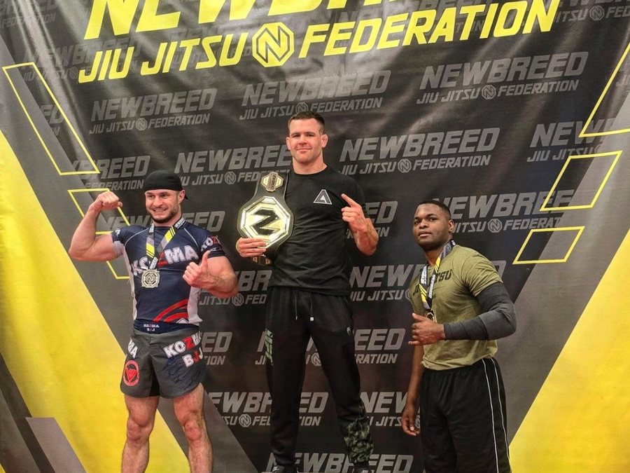 Jonathan Di Lorenzo on the top step of the podium holding a Newbreed Jiu Jitsu Federation title belt